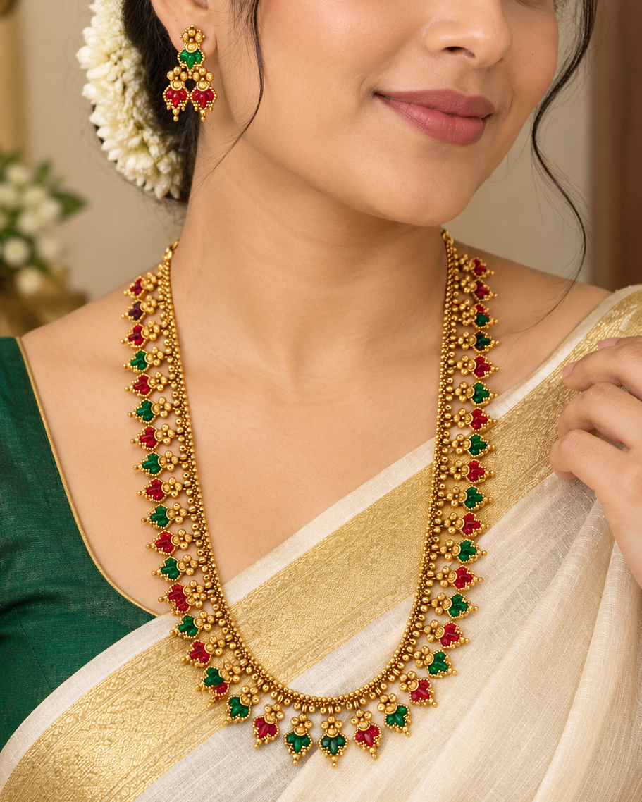 A woman wearing a traditional Indian gold necklace with red and green stones, matching gold earrings, and a green and white saree.