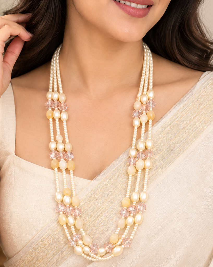 A woman wearing a multi-strand traditional Indian pearl necklace with light pink crystal accents, styled with a cream-colored sari.
