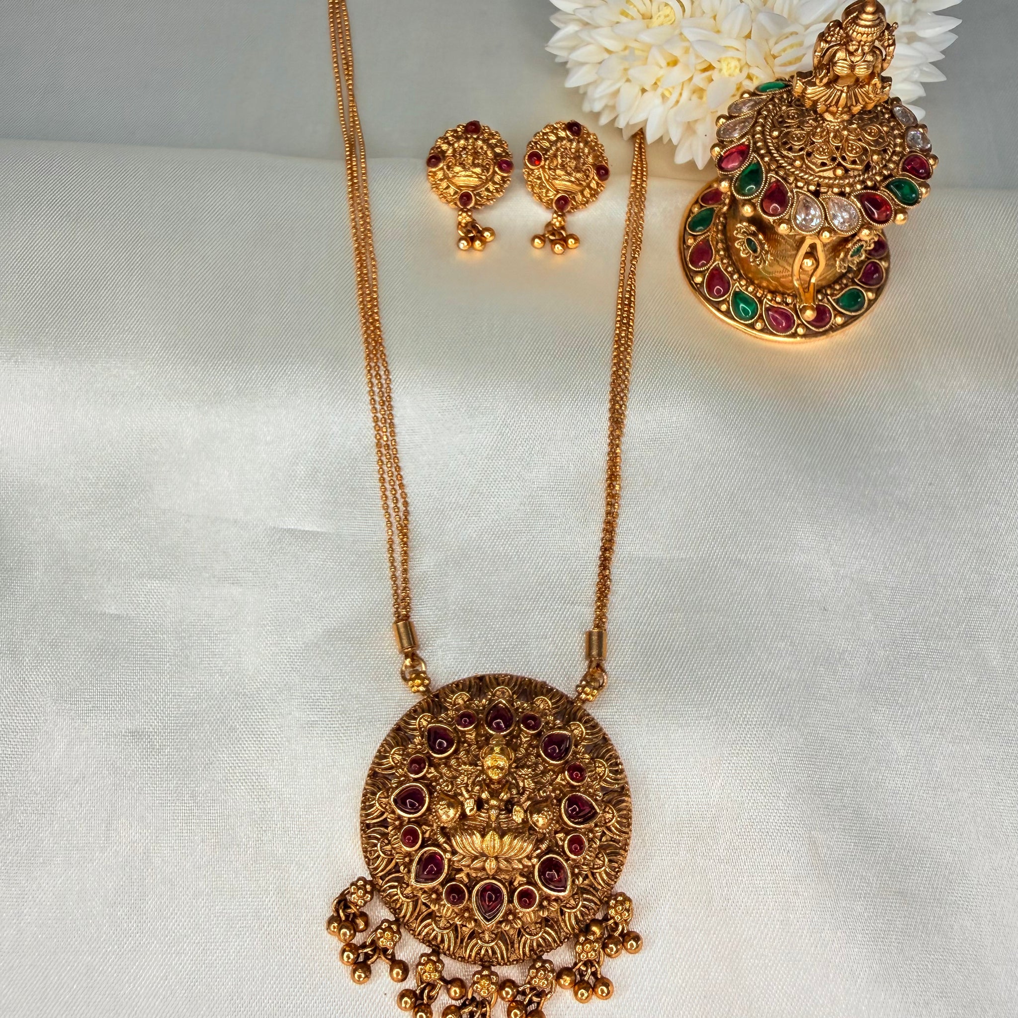 Gold necklace and earrings set with decorative flowers on a white fabric background