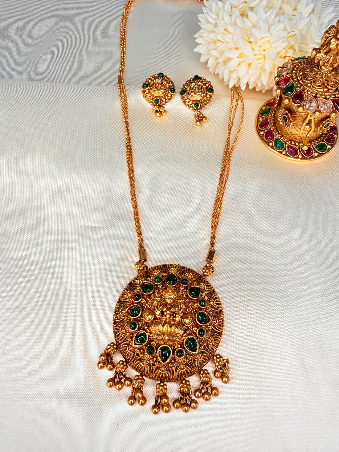 Gold necklace and earrings set with decorative flowers on a white fabric background