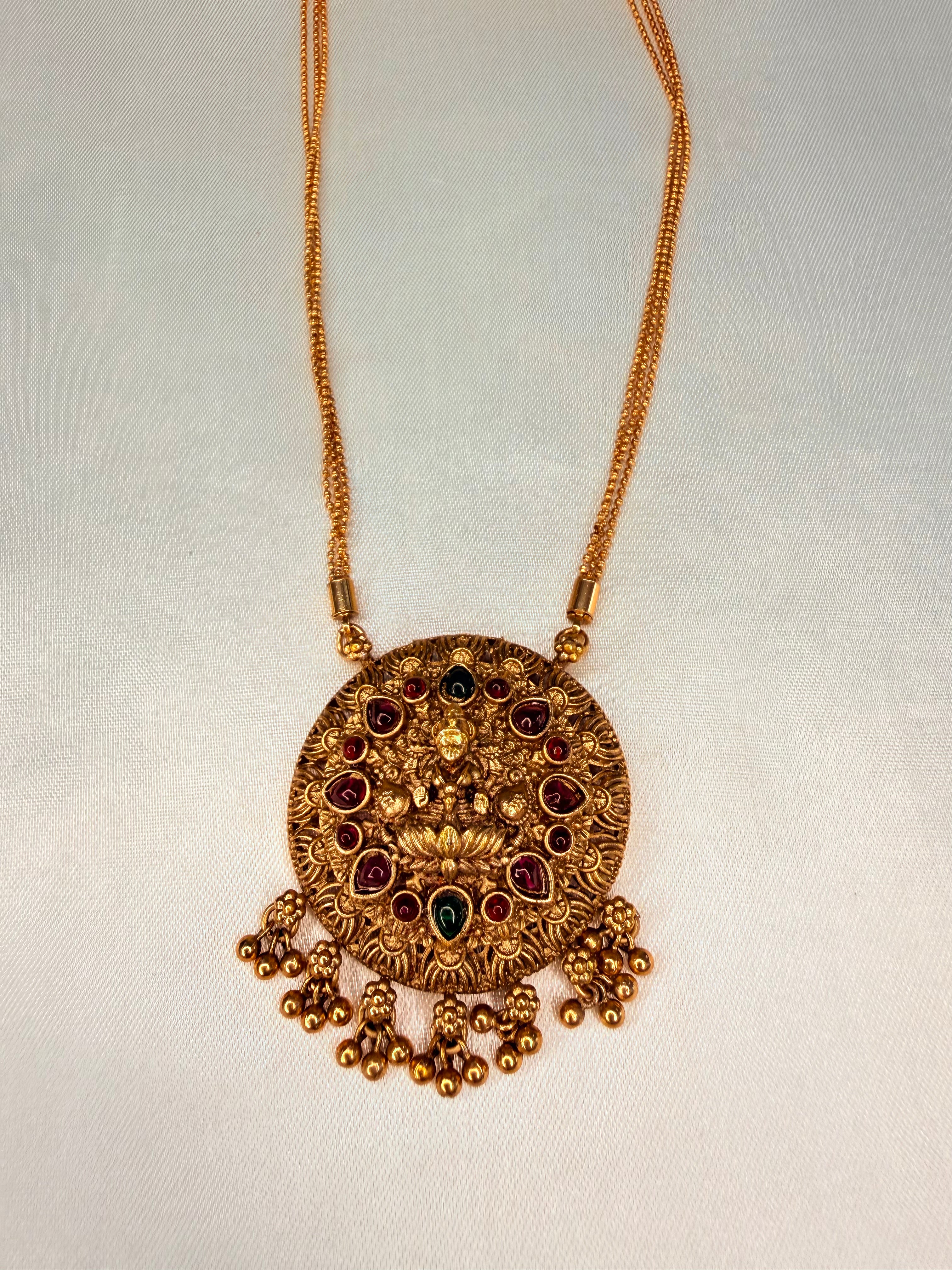 Gold necklace with a decorative pendant on a light gray background