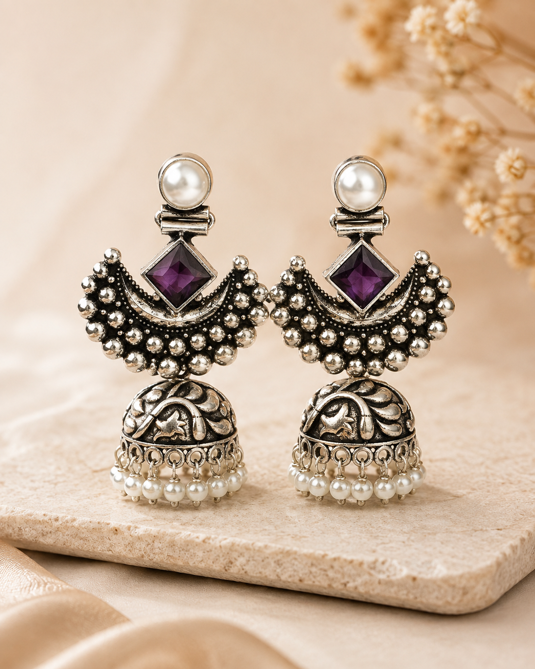 A woman wearing a traditional Indian saree and a matching silver-toned dangle earring with a purple stone and white pearl details.