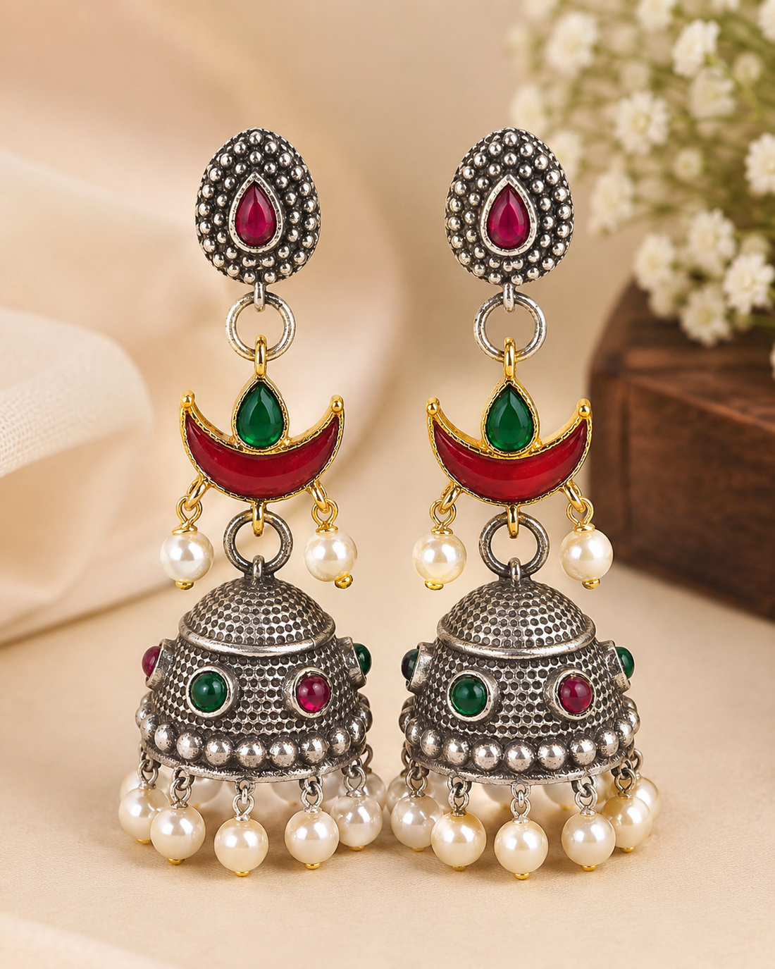 A woman wearing a traditional Indian jhumka earring with silver-toned metal, red and green stones, and white faux pearls, paired with a beige saree.