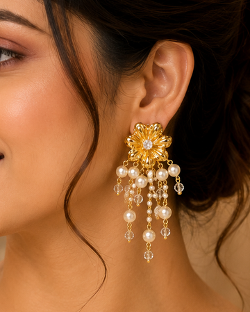 A woman wearing a cream-colored saree with gold embroidery and a matching cream blouse, featuring a prominent gold and pearl chandelier earring.