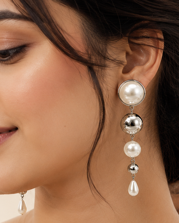 A woman wearing a cream-colored saree and a long, multi-tiered pearl and crystal dangle earring, shown in a close-up profile view.