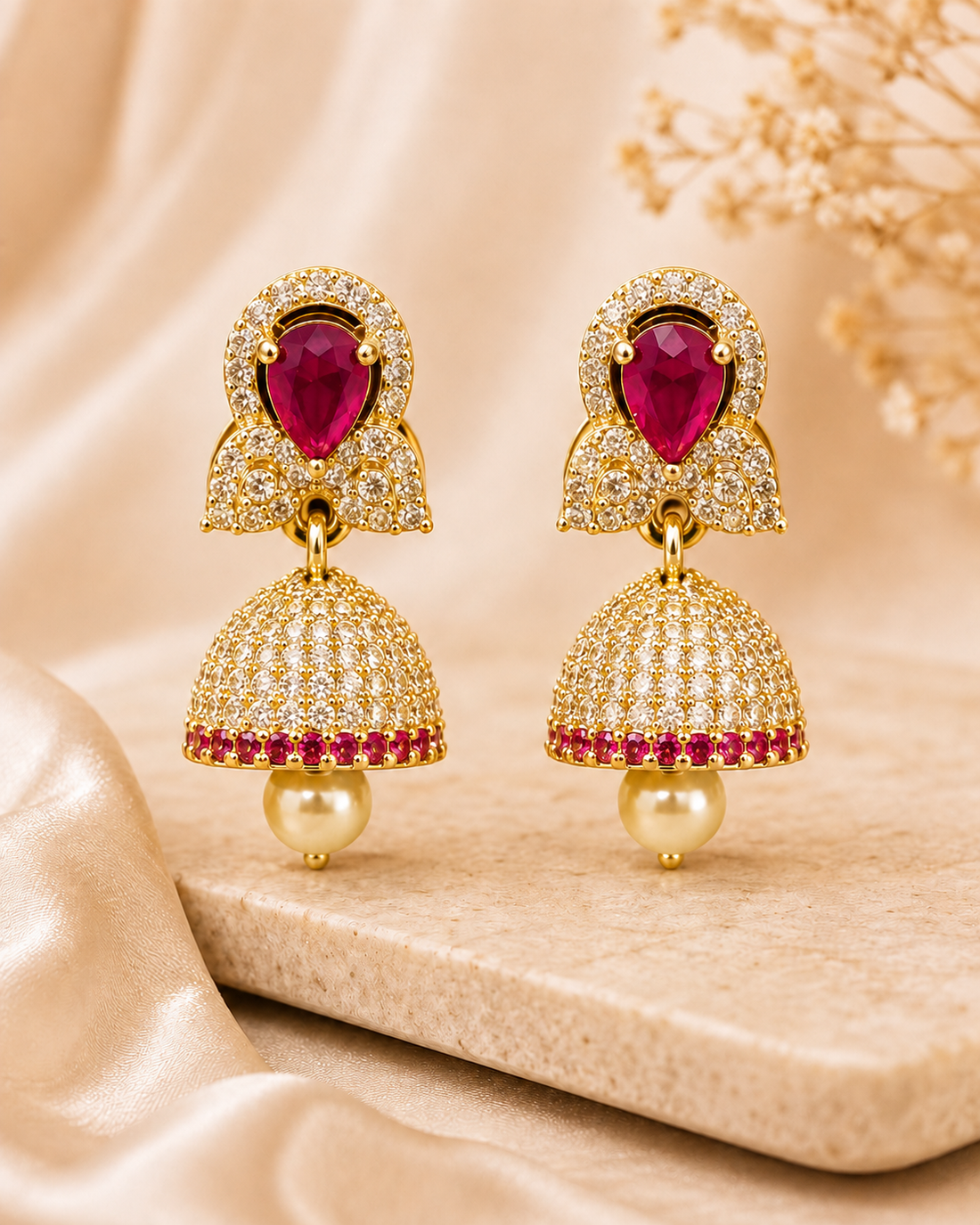 A woman wearing a cream-colored saree and matching cream jewelry, featuring a prominent gold-toned jhumka earring with a green stone and pearl drop.