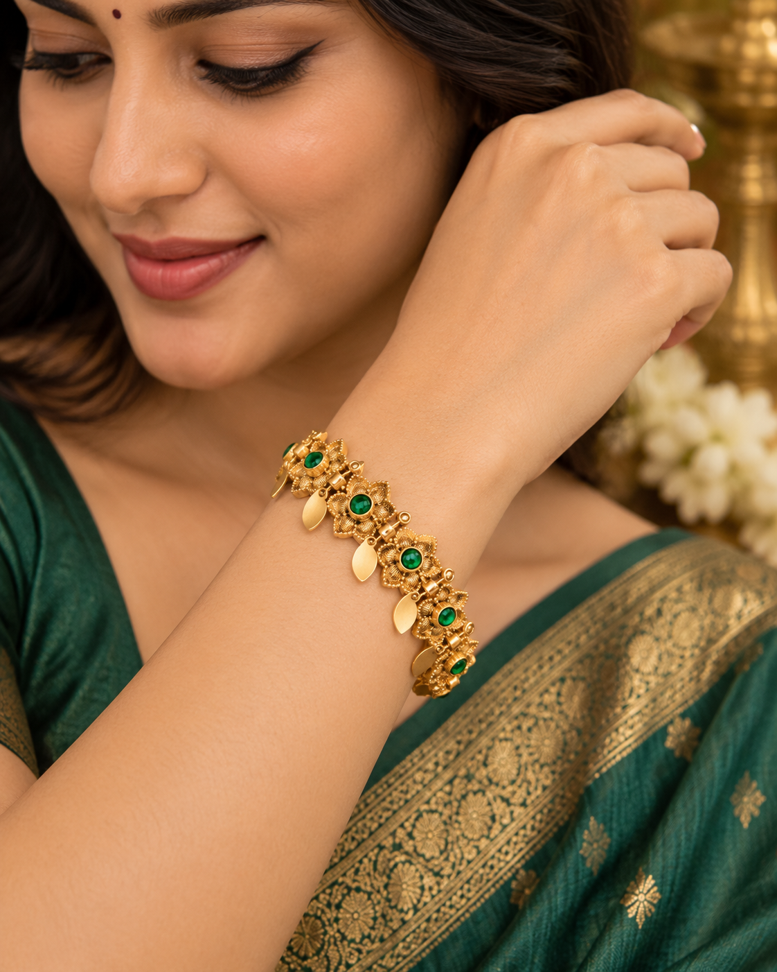 A woman wearing a green and gold saree with a gold-toned bracelet featuring green stone accents, shown in a close-up lifestyle shot.