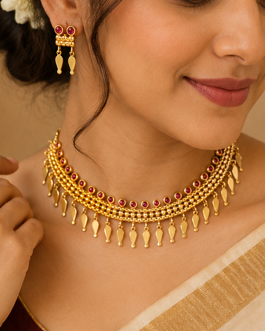 A woman wearing a traditional Indian outfit with a cream and gold saree, a maroon blouse, a gold necklace, matching earrings, and a gold bracelet, with white flowers in her hair.