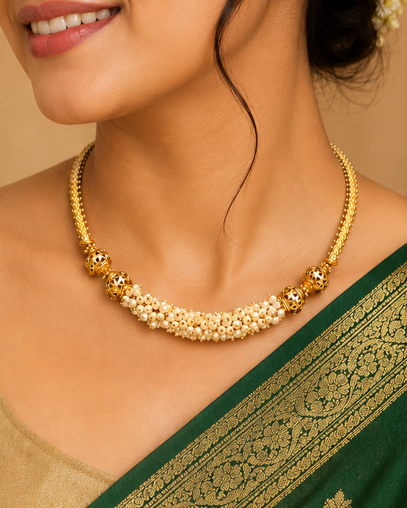 A woman wearing a gold floral choker necklace with small gold and white stones, paired with a green and gold saree. She is shown in a warm, traditional indoor setting with a carved wooden screen in the background.