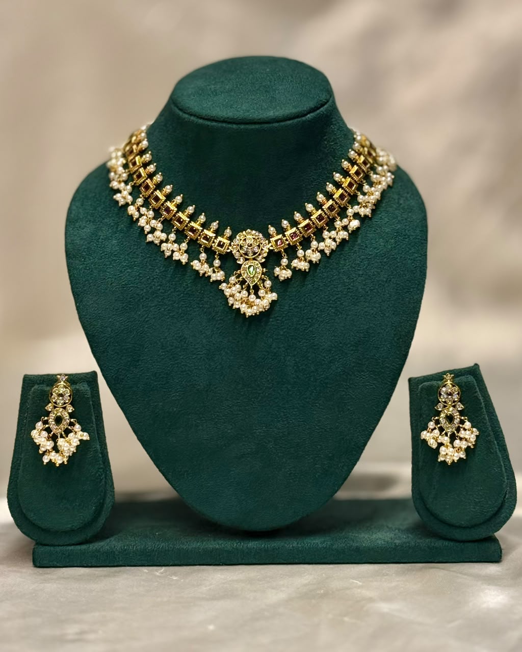 Gold and white stone jewelry set displayed on a dark green velvet jewelry bust, including a choker necklace, matching earrings, and a small stand, against a neutral beige background.