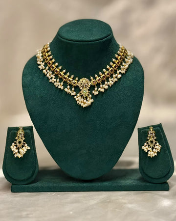 Gold and white stone jewelry set displayed on a dark green velvet jewelry bust, including a choker necklace, matching earrings, and a small stand, against a neutral beige background.