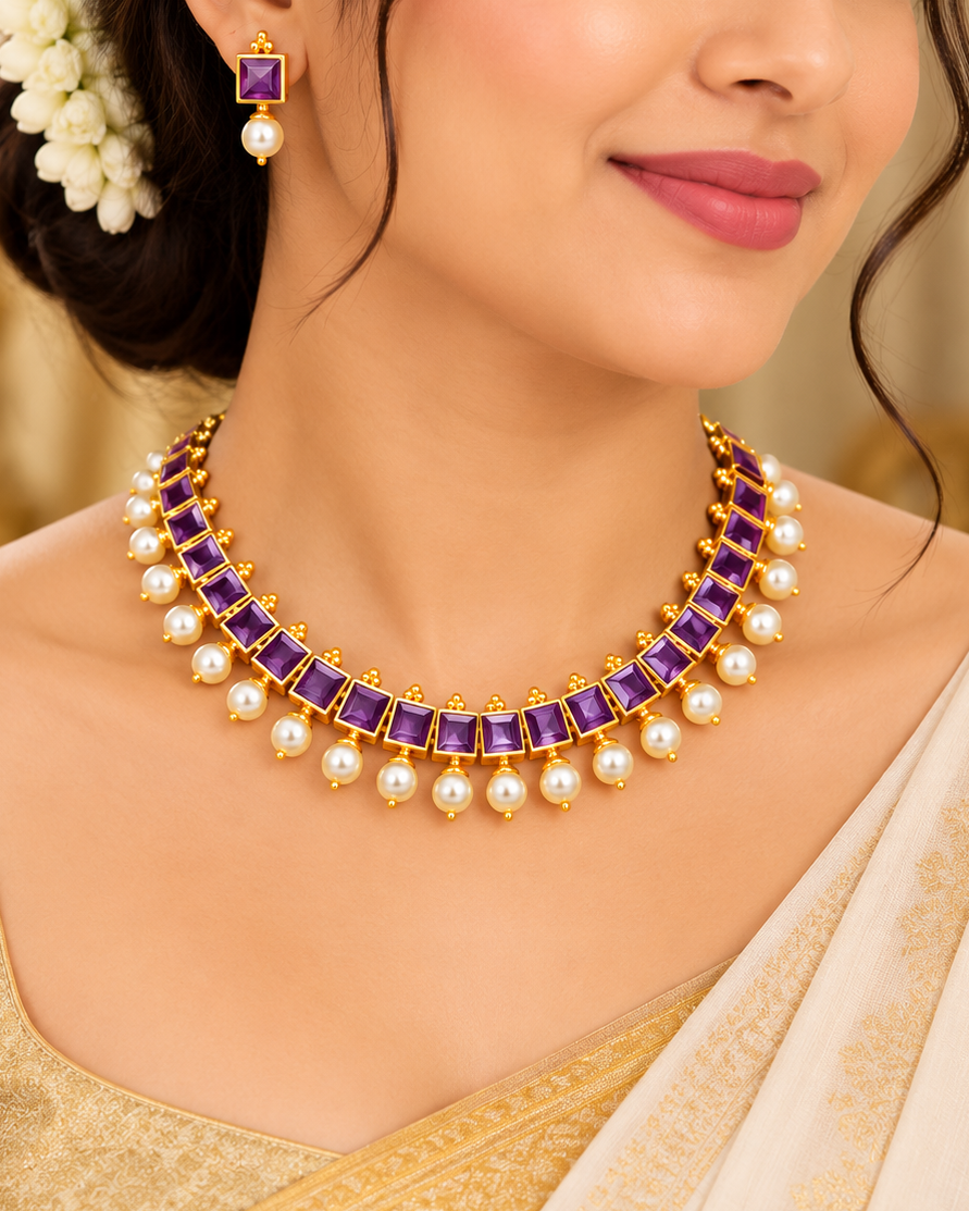 A woman wearing a gold-plated traditional necklace with purple rectangular stones and white pearls, along with matching purple and pearl earrings, styled with a cream and gold saree.