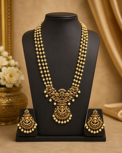 Gold and cream-colored traditional Indian jewelry set featuring a double-strand pearl necklace with an ornate gold pendant, matching drop earrings, and a black display stand.