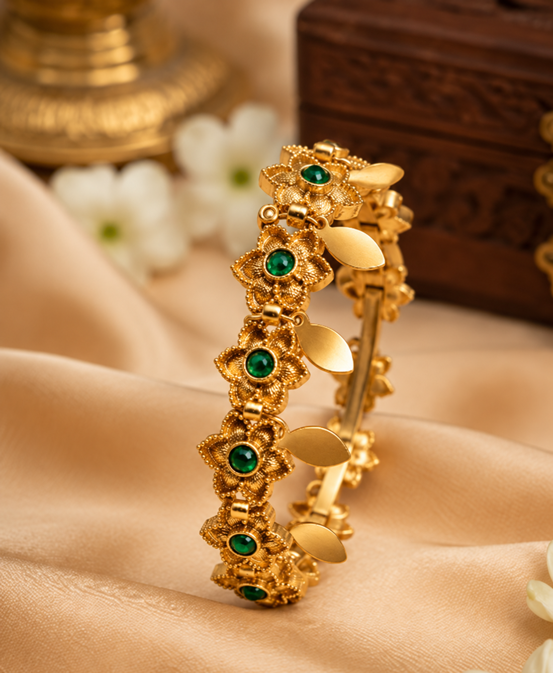A woman wearing a green and gold saree with a gold-toned bracelet featuring green stone accents, shown in a close-up lifestyle shot.