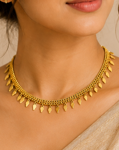 A woman wearing a gold chain necklace with small teardrop-shaped pendant charms and matching gold stud earrings, styled with a beige sari.