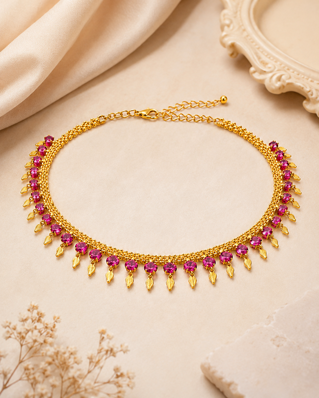 A woman wearing a gold-toned choker necklace with red gemstone accents, styled with a beige sari against a soft beige background.