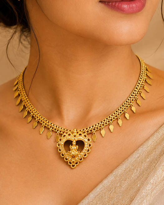 A woman wearing a gold heart-shaped pendant necklace and matching stud earring, styled with a shimmering beige sari against an elegant, softly lit background.
