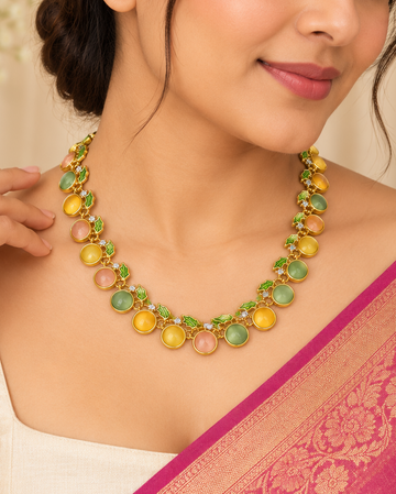 A woman wearing a gold-plated necklace with round green, yellow, and pink stones, paired with a pink and gold sari.