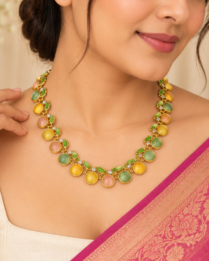 A woman wearing a gold-plated necklace with round green, yellow, and pink stones, paired with a pink and gold sari.
