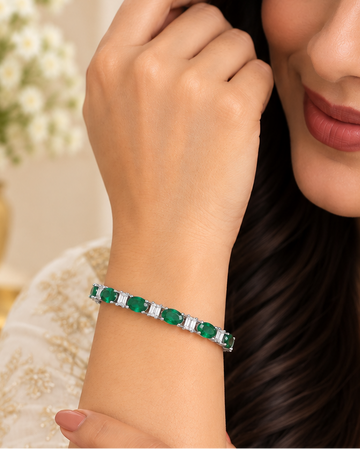 A woman wearing a silver-toned bangle bracelet with green rectangular stones and small white accent stones, shown in a close-up lifestyle shot.