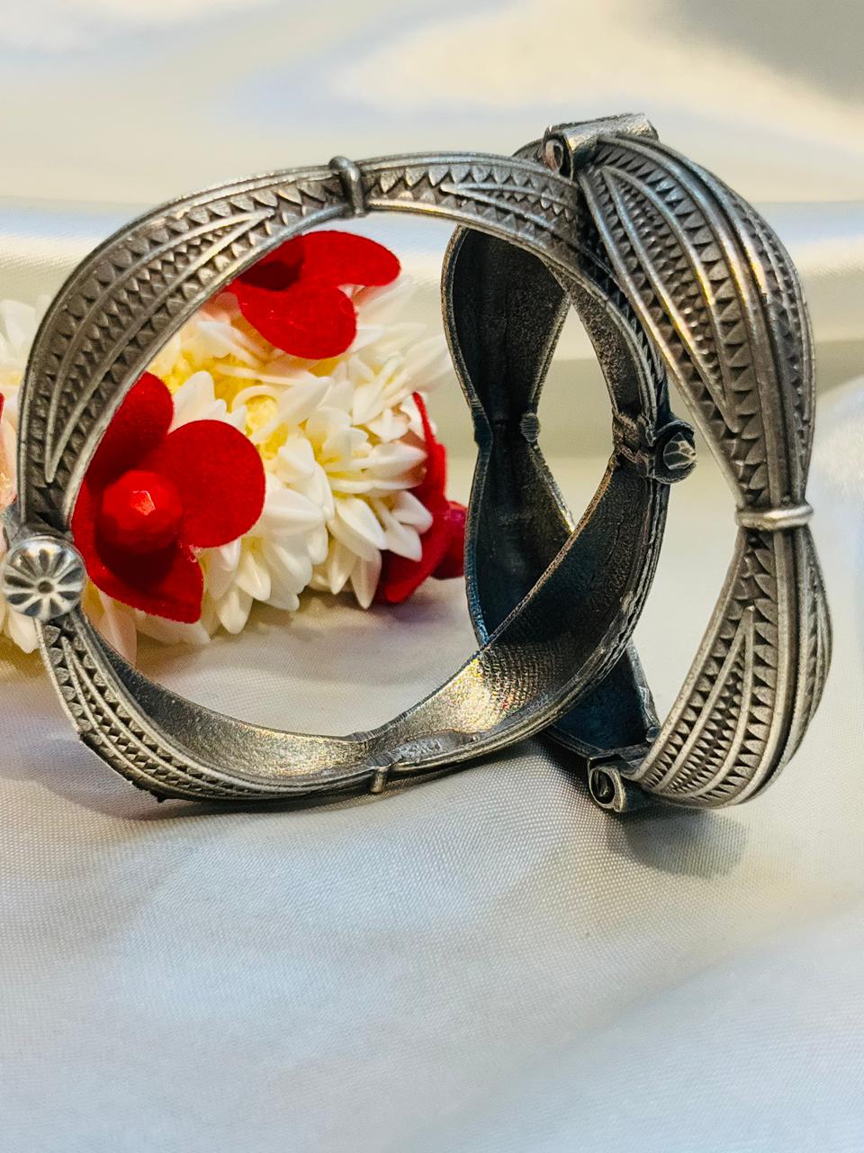Silver bangles with intricate designs on a white fabric background