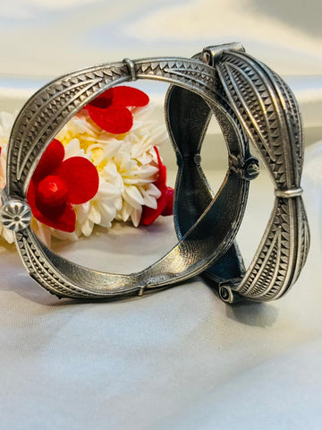 Silver bangles with intricate designs on a white fabric background