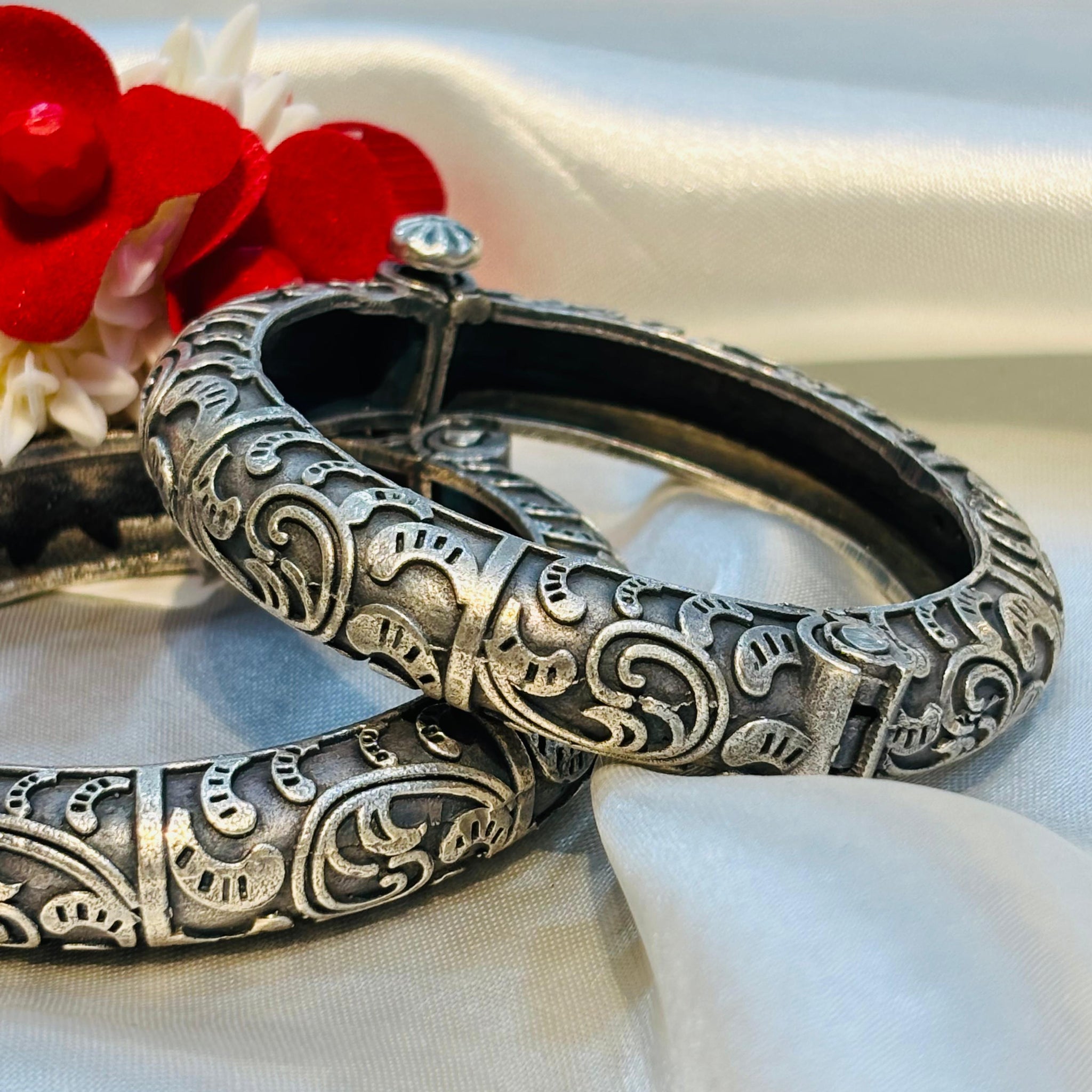 Silver bangles with intricate designs on a white fabric background