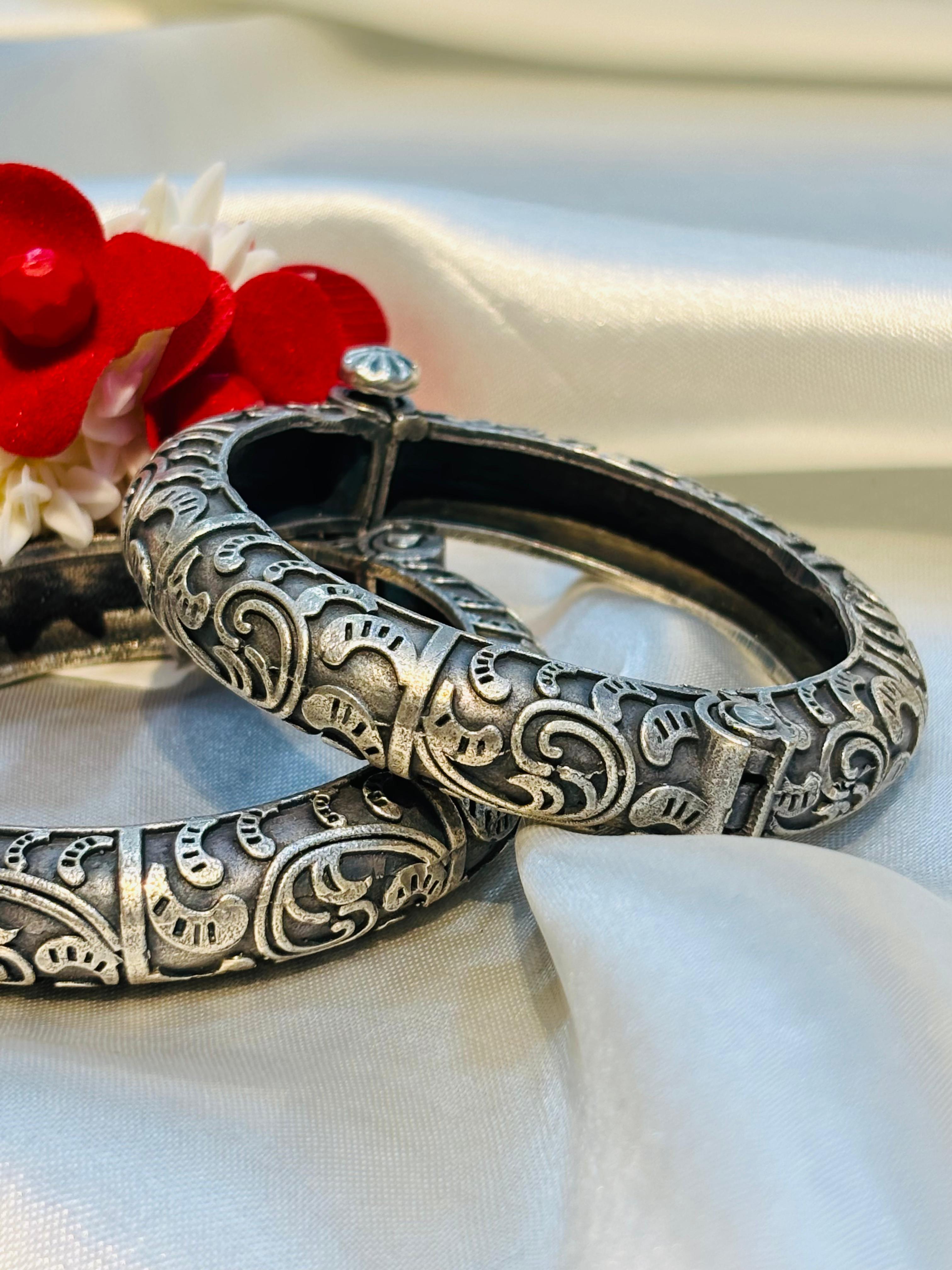 Silver bangles with intricate designs on a white fabric background