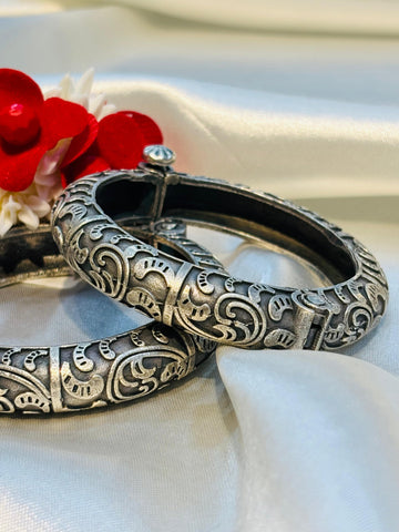 Silver bangles with intricate designs on a white fabric background