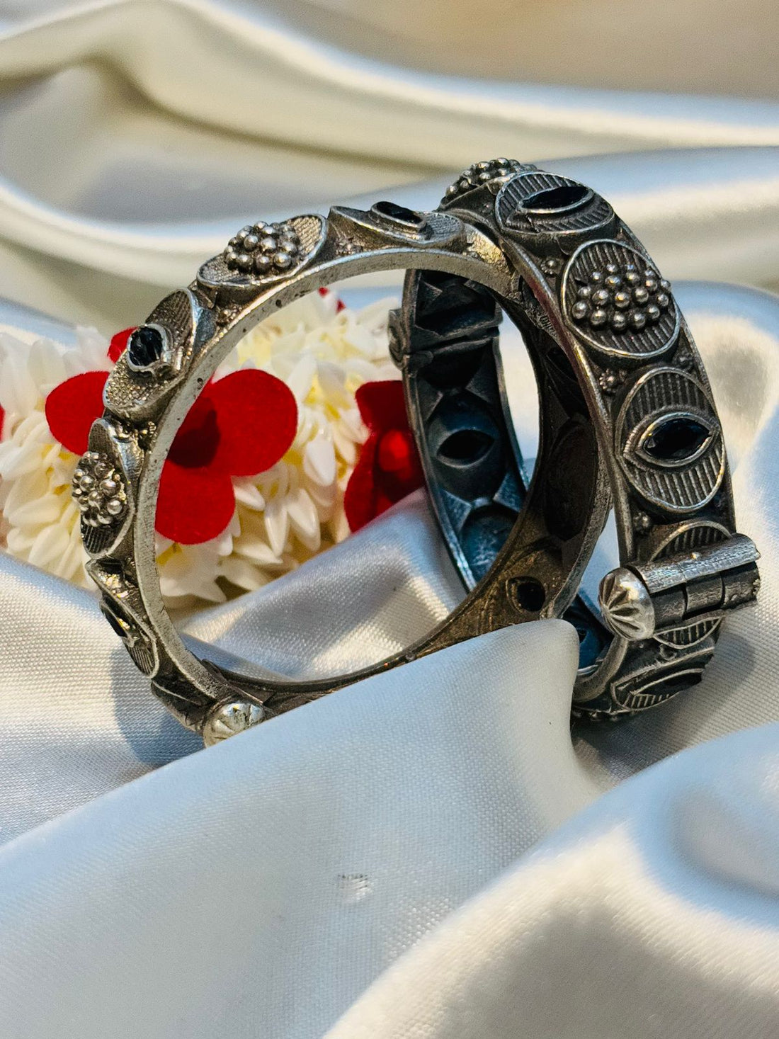 Two silver bracelets with intricate designs on a white fabric background with red flowers.