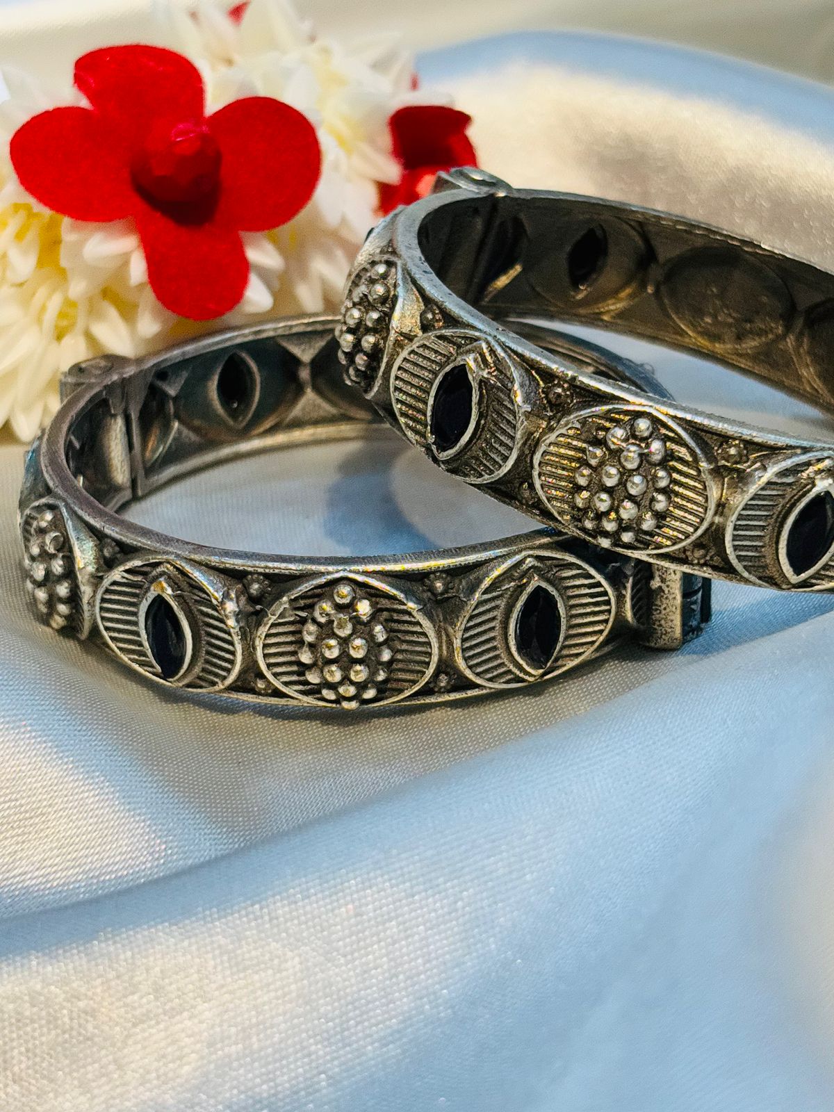 Two silver bracelets with intricate designs on a white fabric background with red flowers.