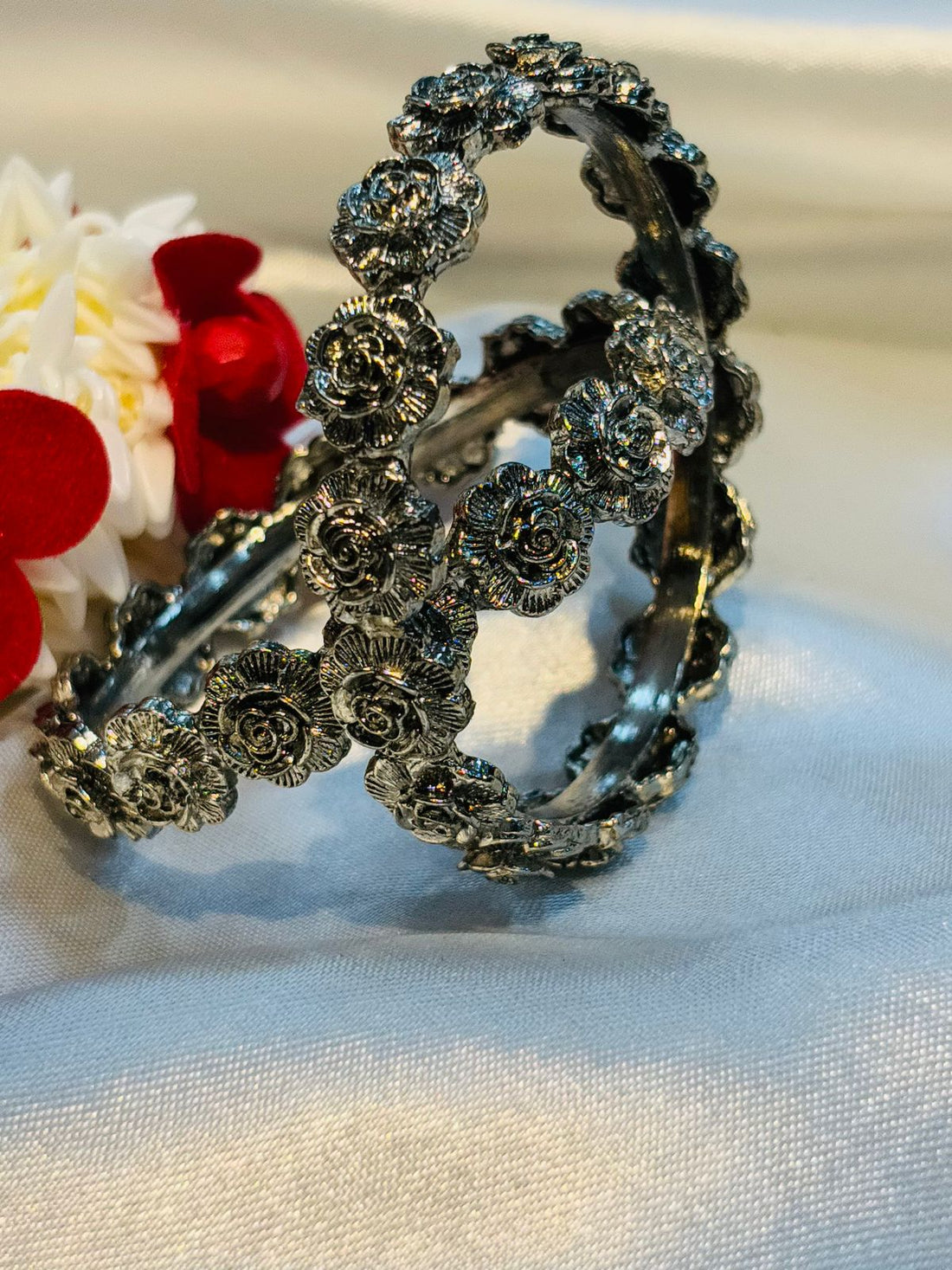 Decorative silver bangle with floral patterns on a white fabric background