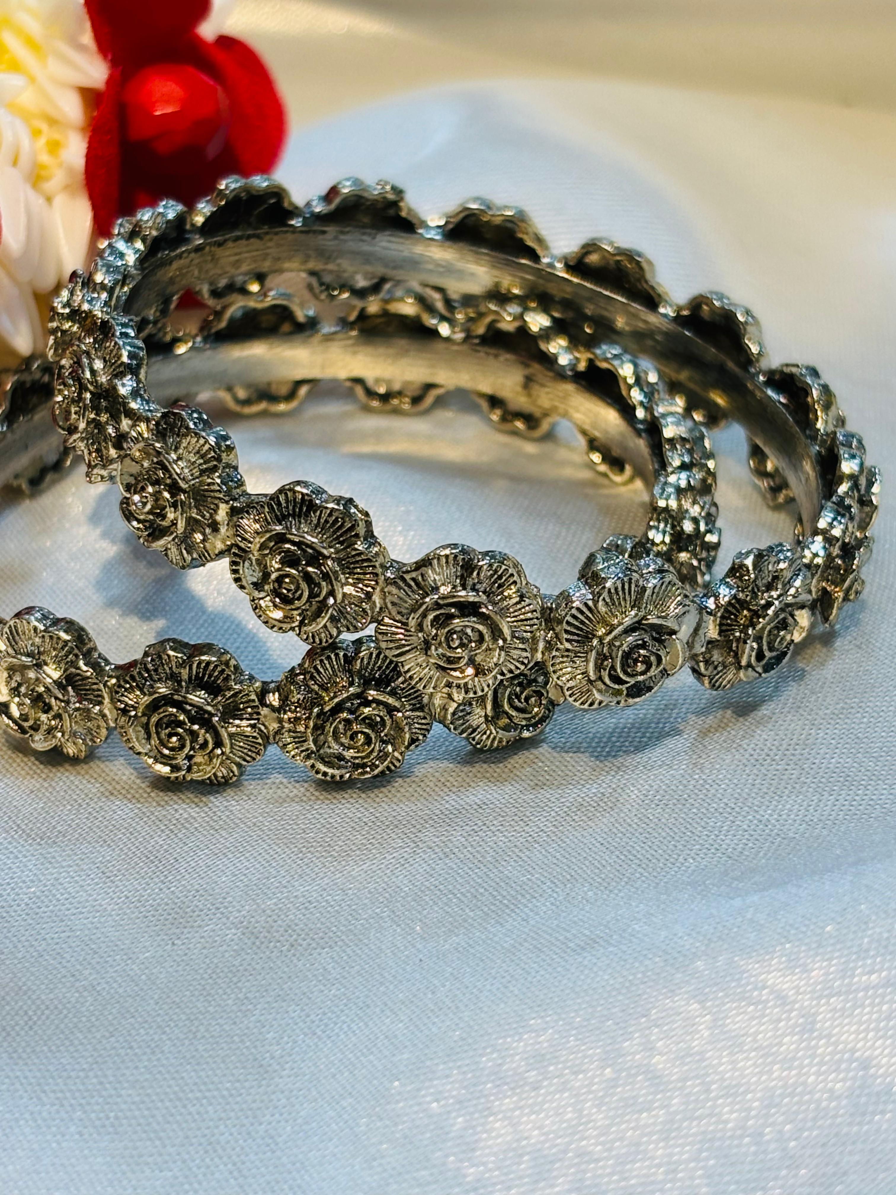 Decorative silver bangle with floral patterns on a white fabric background