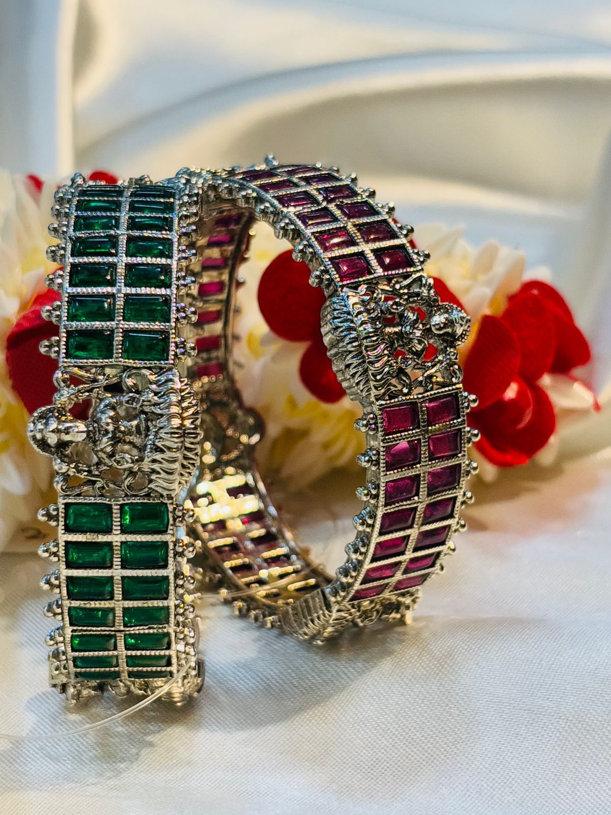 Decorative bracelet with green and red gemstones on a white fabric background