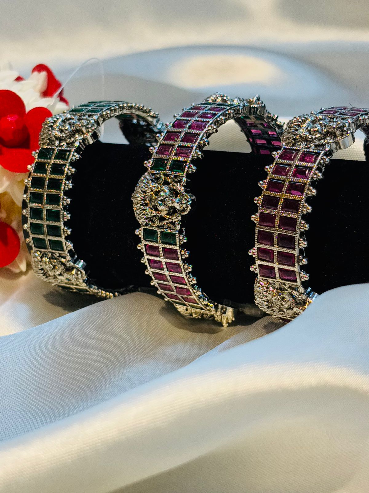 Decorative headbands with gemstone patterns on a white surface with red flowers in the background