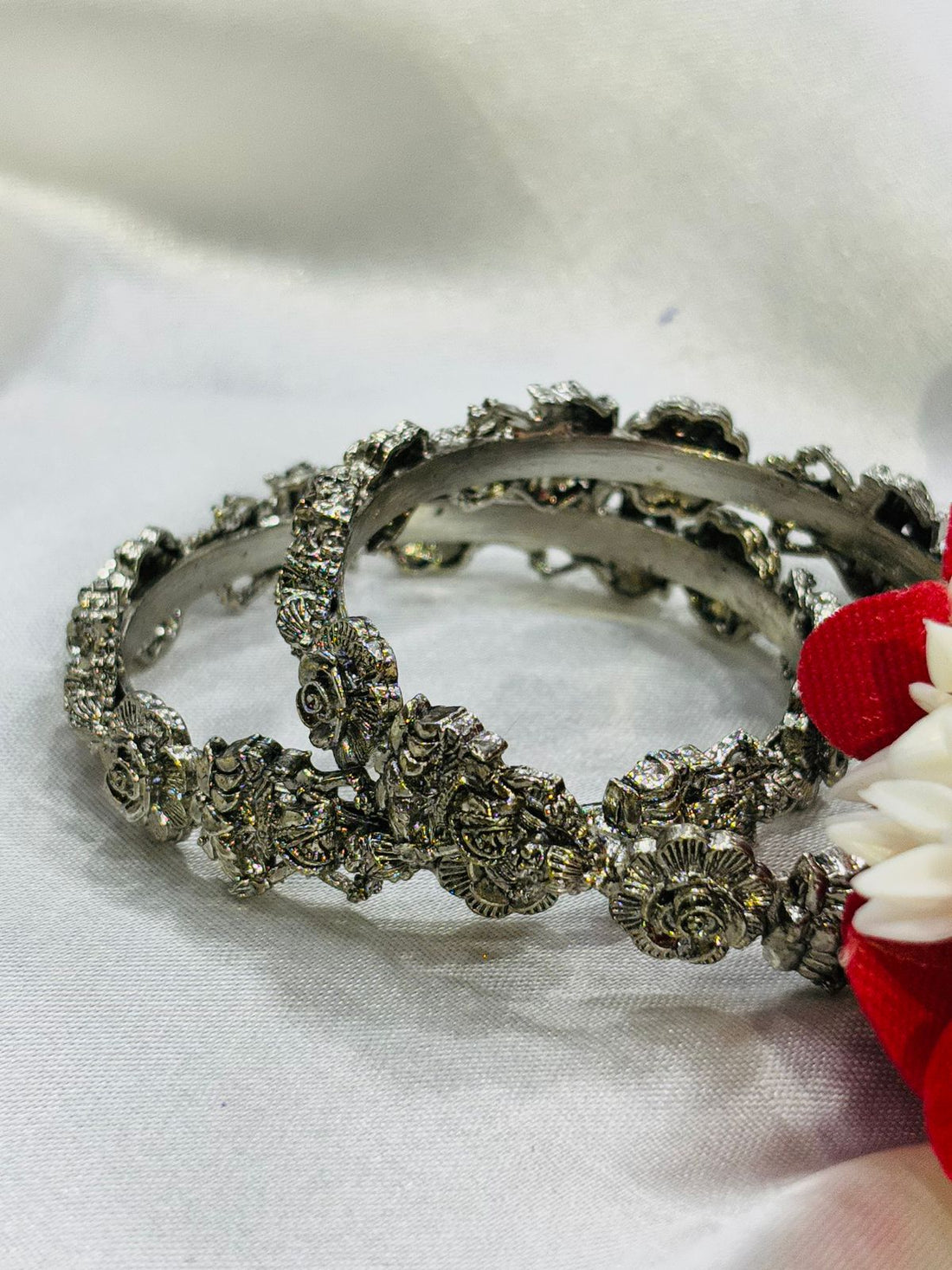 Silver hoop earrings with floral designs on a white fabric background