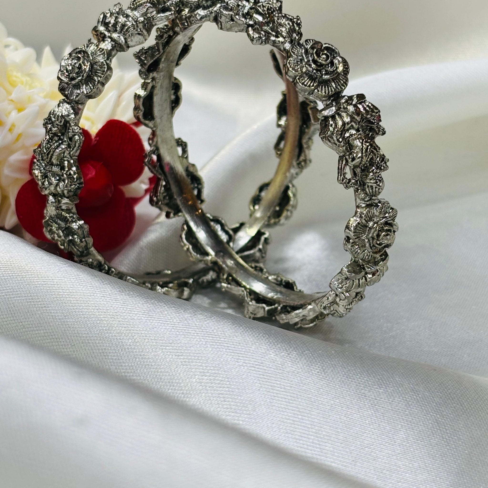Silver hoop earrings with floral designs on a white fabric background