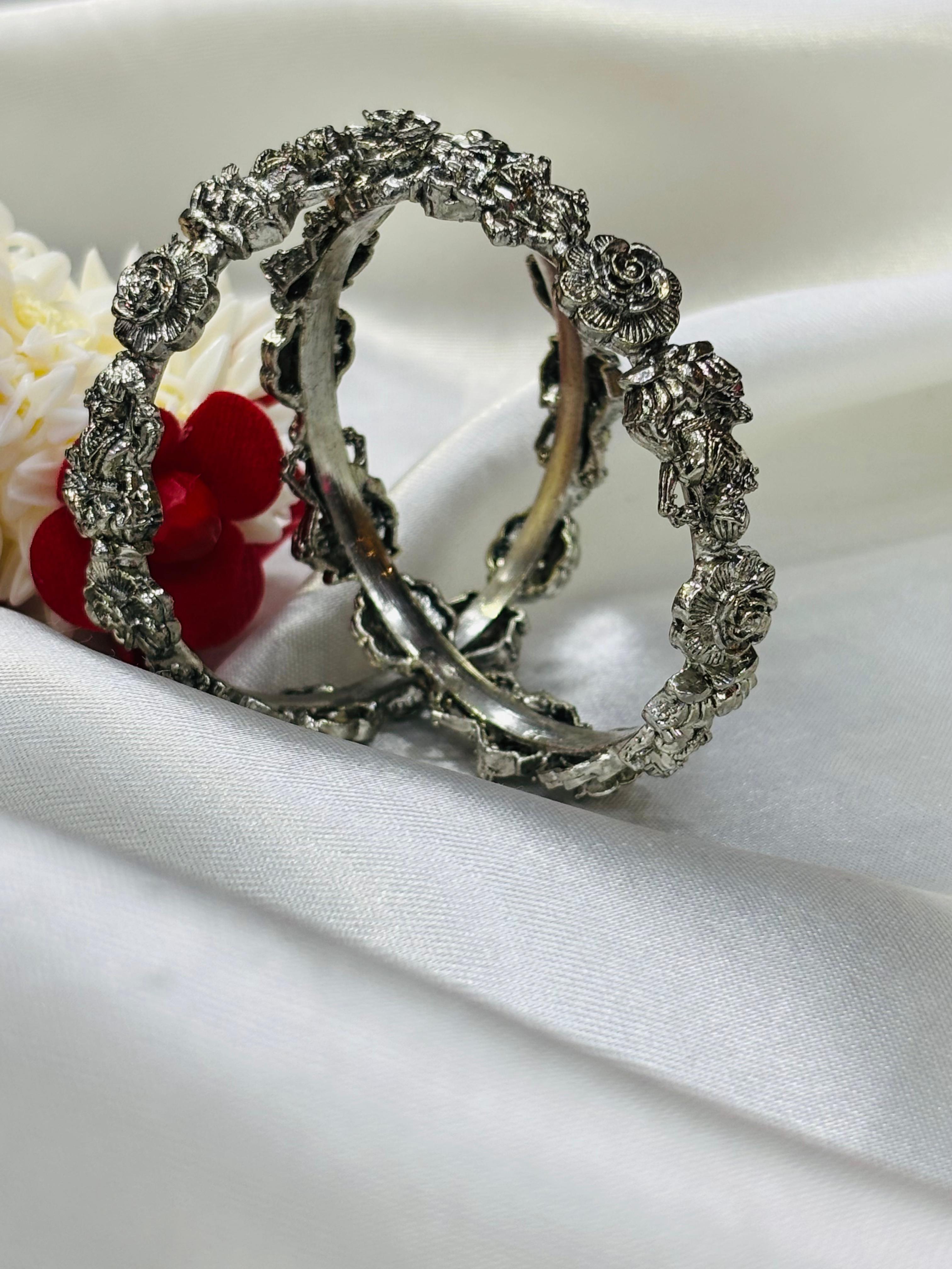 Silver hoop earrings with floral designs on a white fabric background