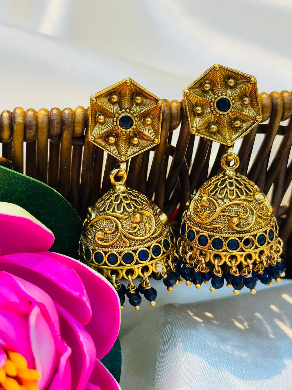 Gold and blue earrings on a wooden comb with a pink flower in the background