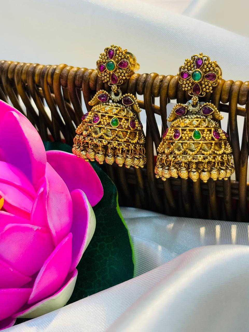 Gold earrings with gemstones on a decorative stand with a pink flower and green leaves.