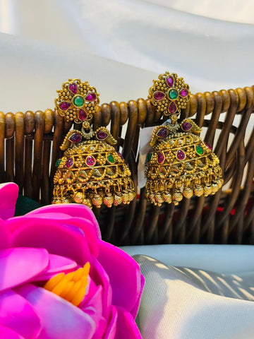 Gold earrings with gemstones on a wicker surface with a pink flower in the foreground.