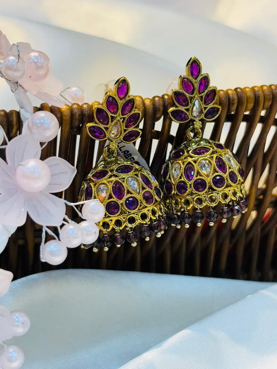 Gold and purple earrings with floral decorations on a white surface