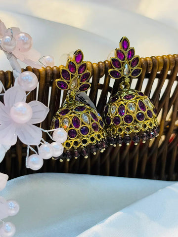 Gold and purple earrings with floral decorations on a white surface