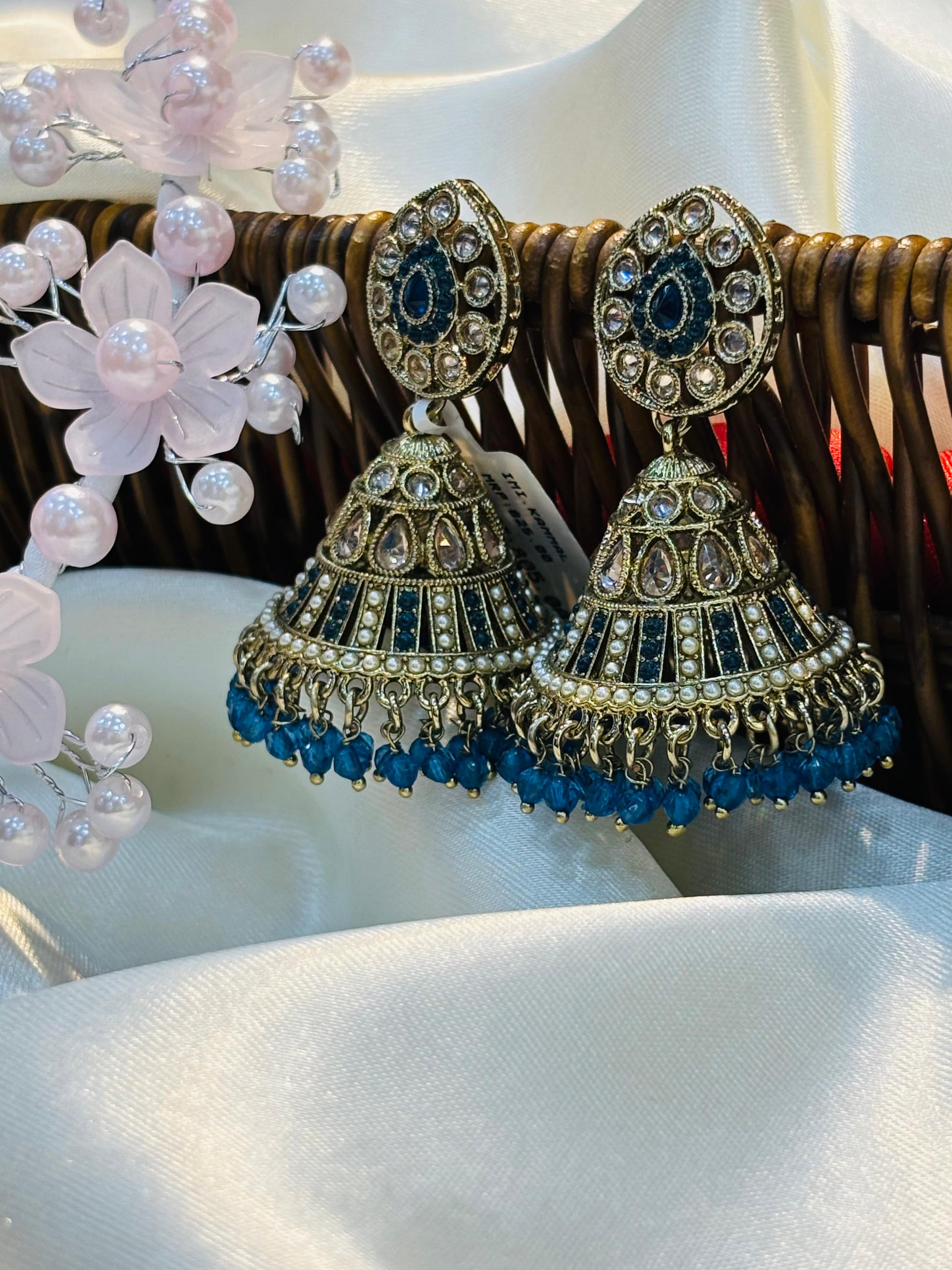 Pair of ornate earrings with blue beads on a white surface with flowers.