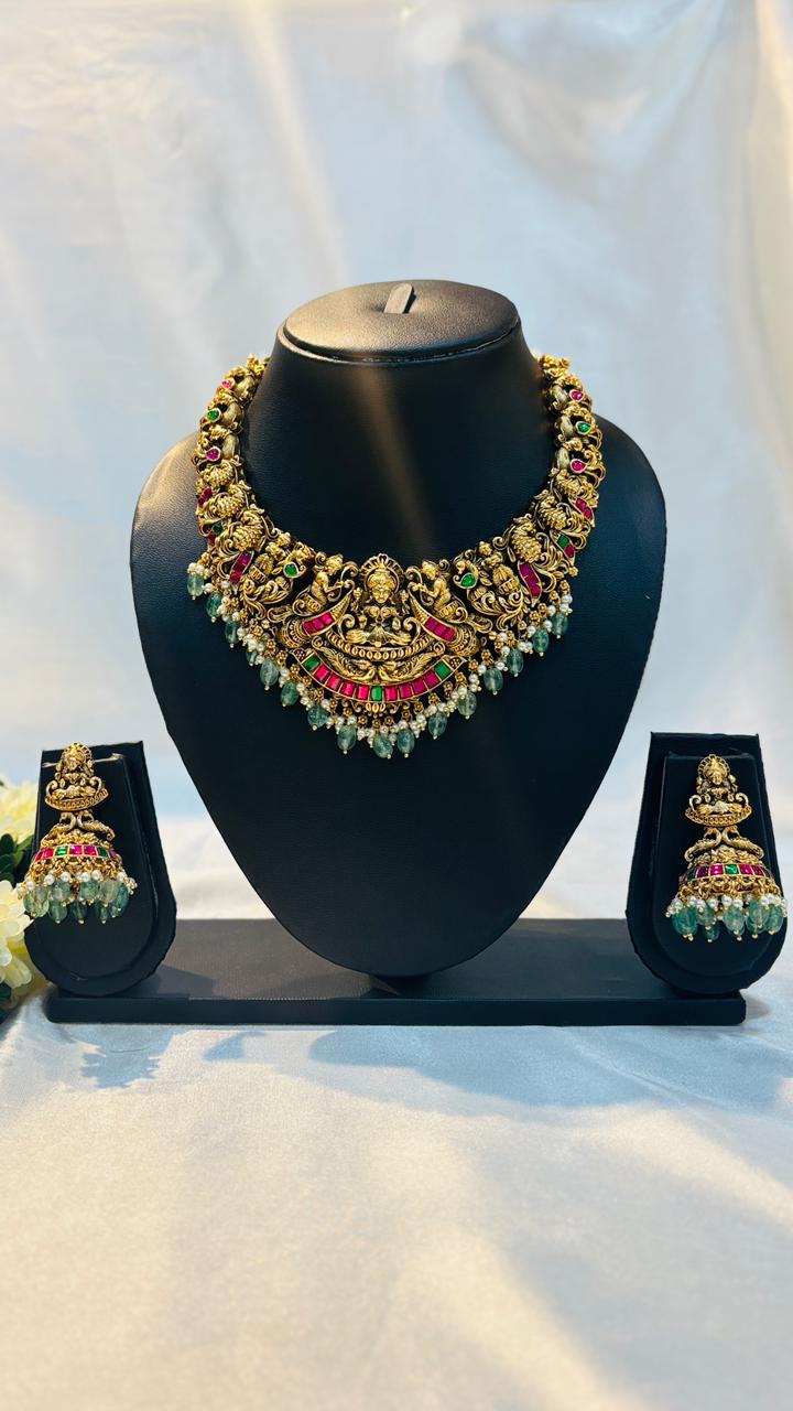 Ornate necklace and earrings set on a black stand against a white background