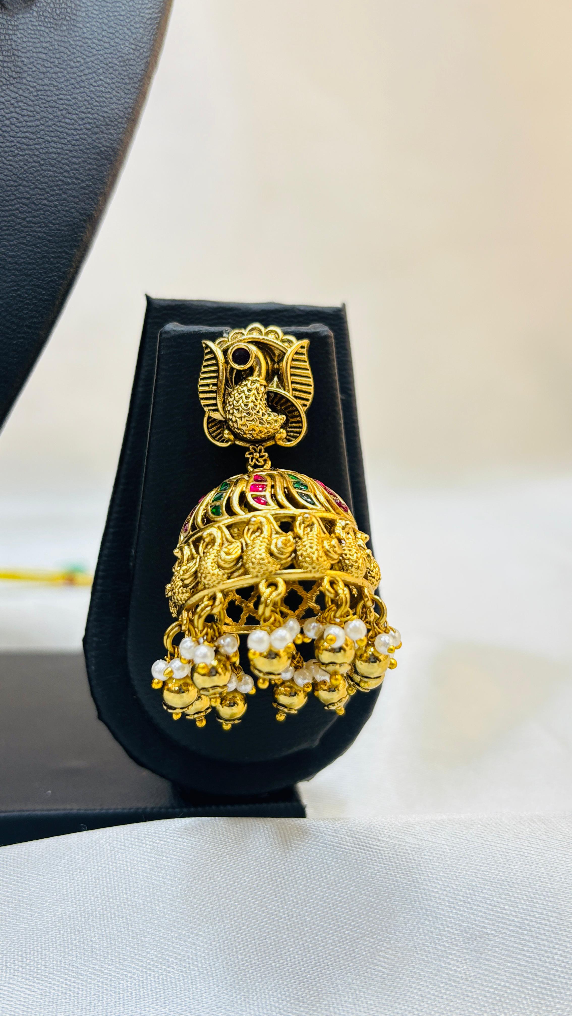 Gold jhumka earring on a black display stand with a white background