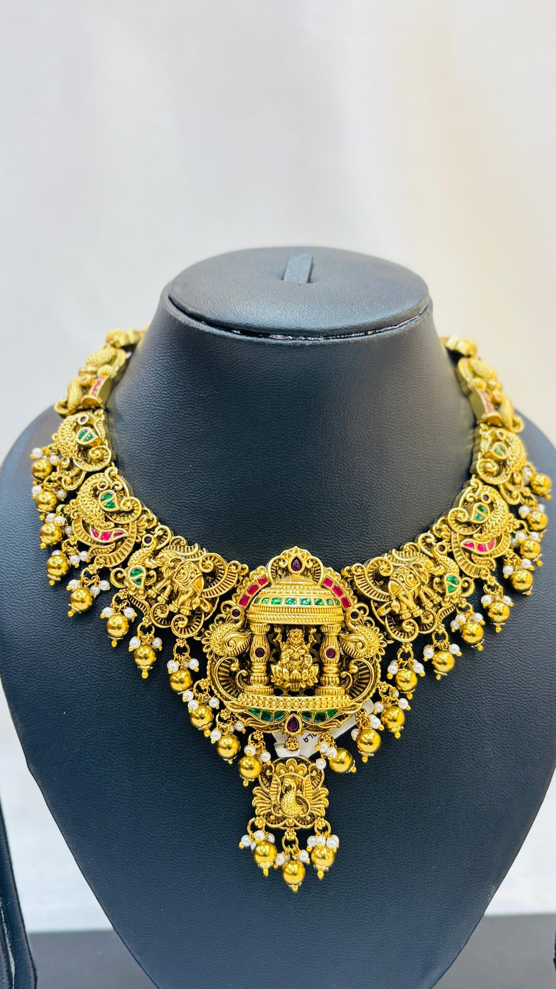 Gold necklace and earrings set on a black mannequin against a white background