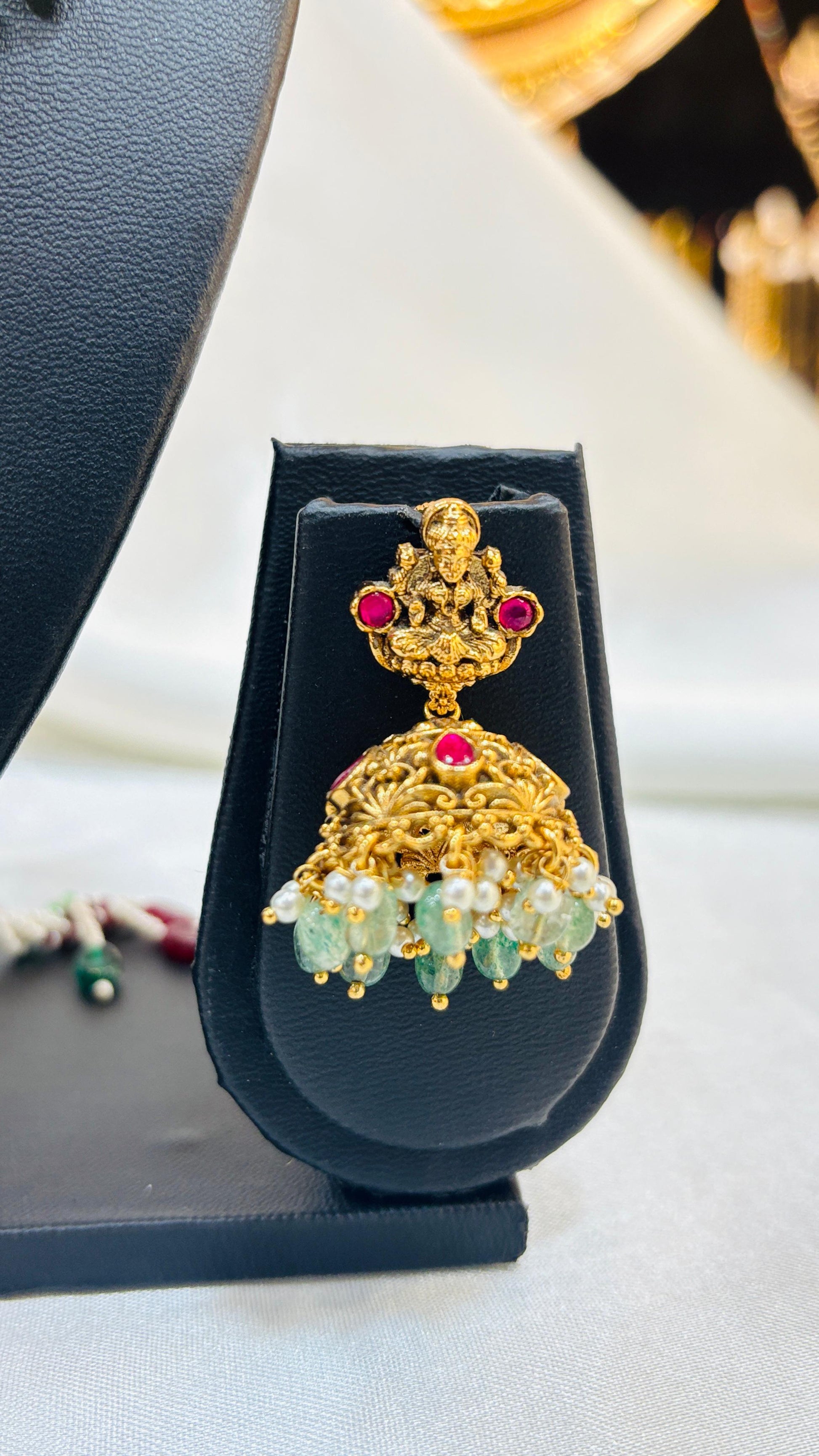 Gold earring with gemstones on a black stand