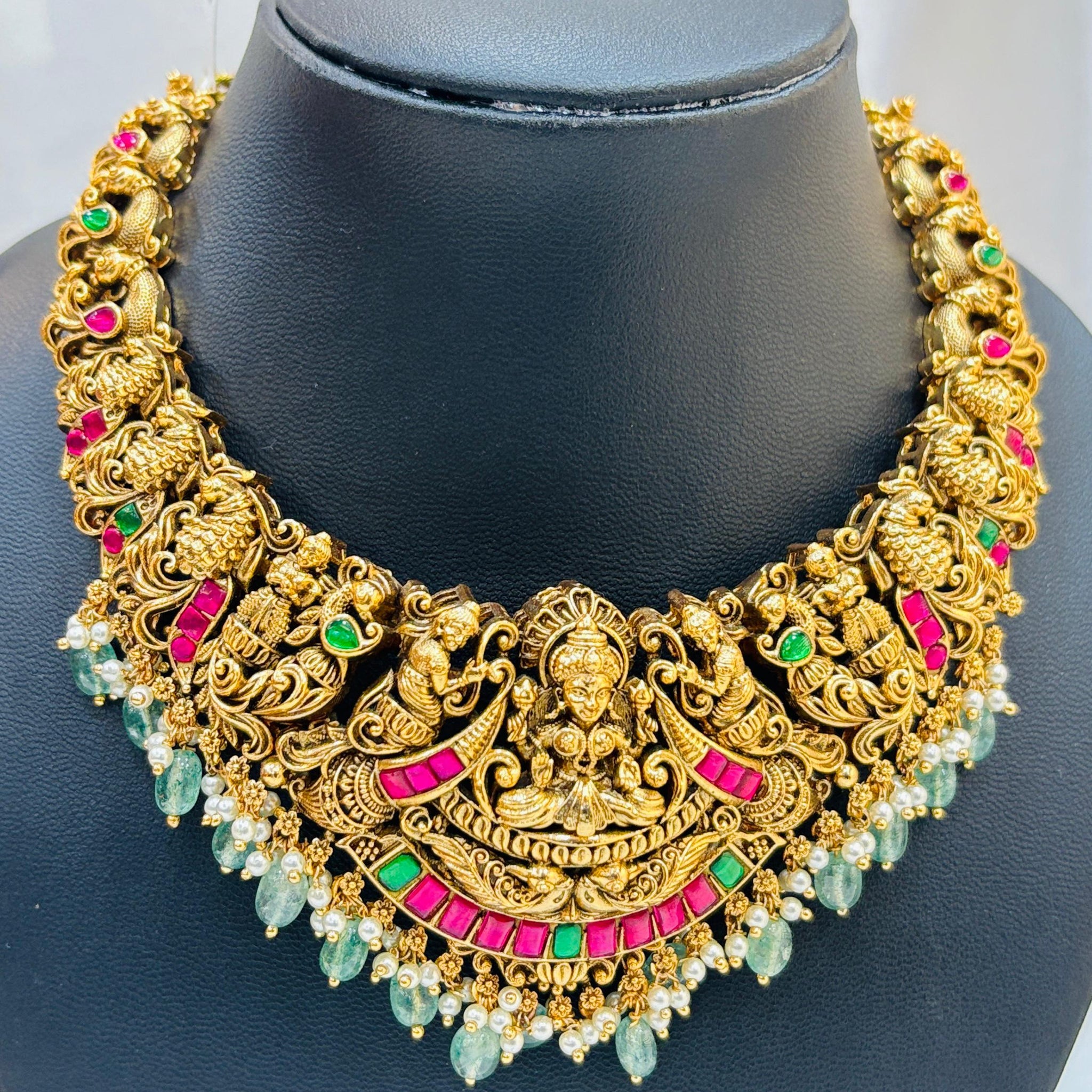Gold necklace with colorful stones on a black mannequin bust