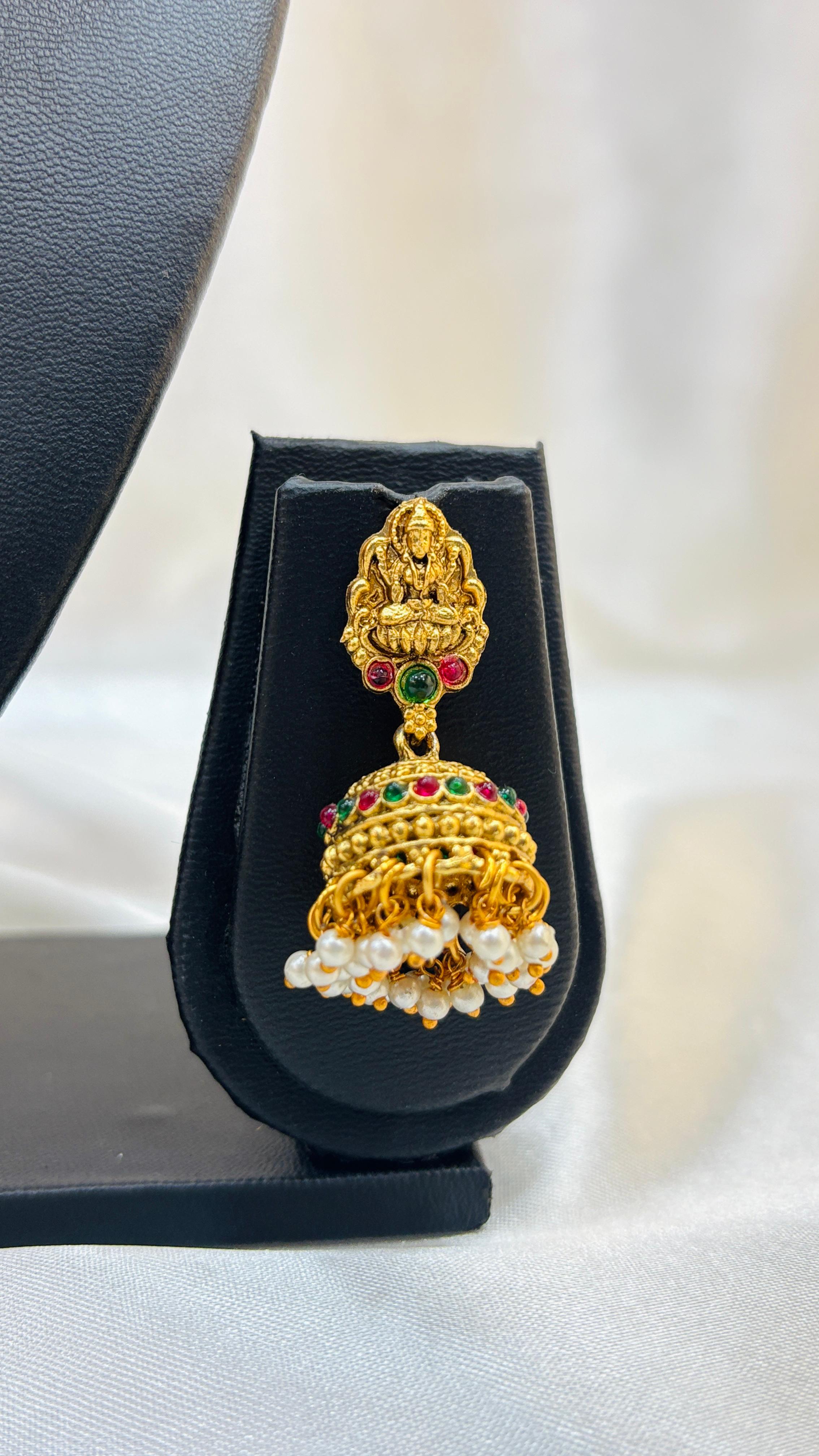 Gold jhumka earring with pearls and gemstones on a black stand.